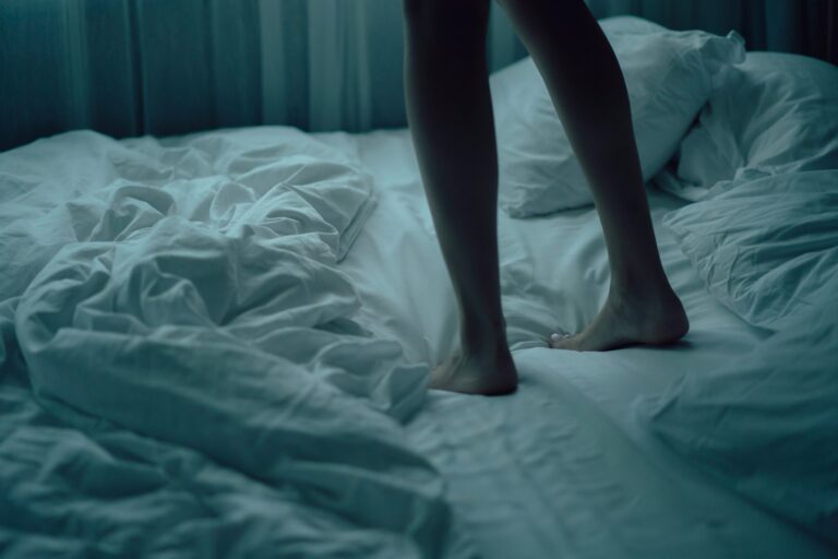 Piernas persona sonámbula de pie encima de la cama.