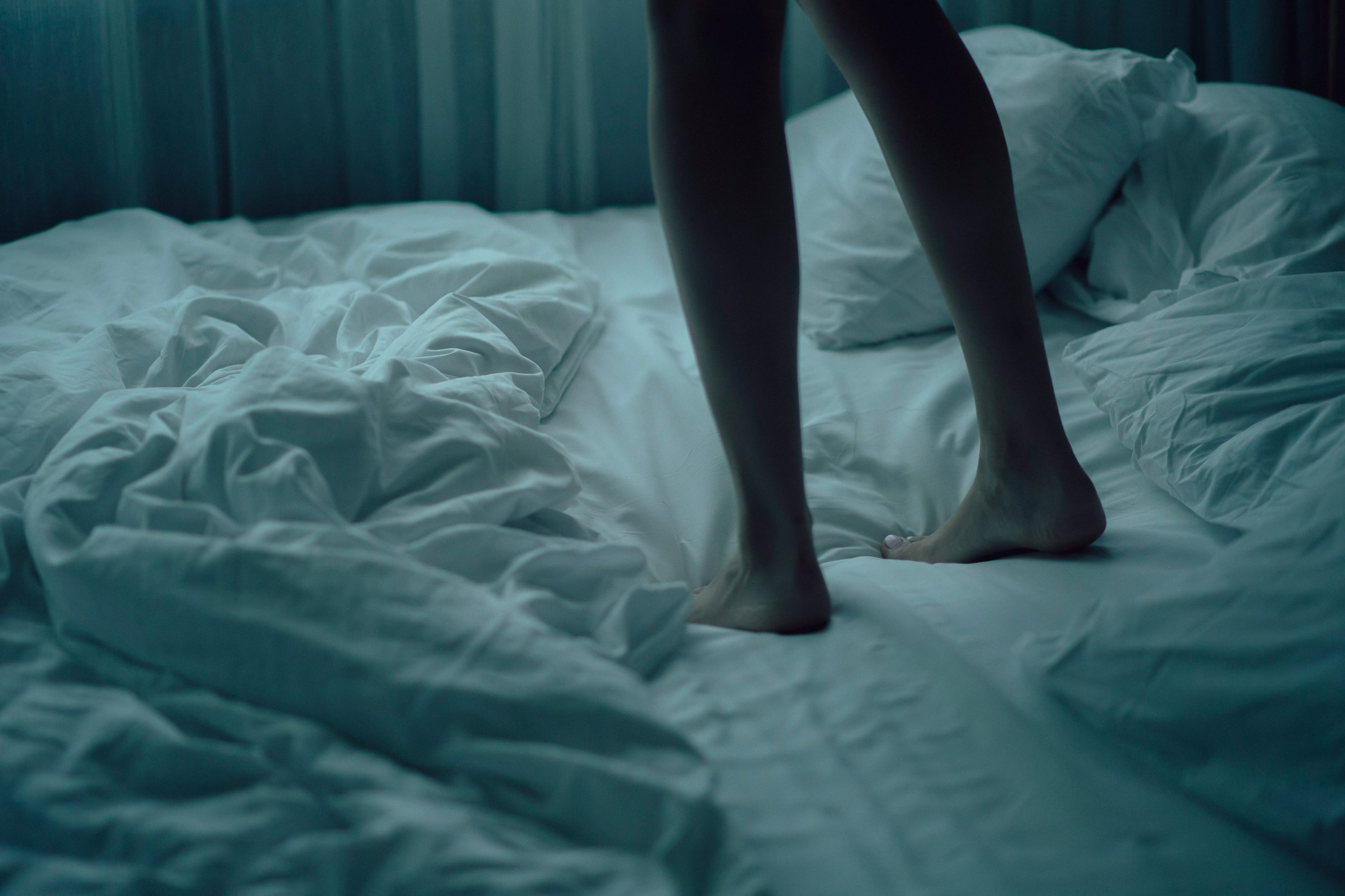 Piernas persona sonámbula de pie encima de la cama.